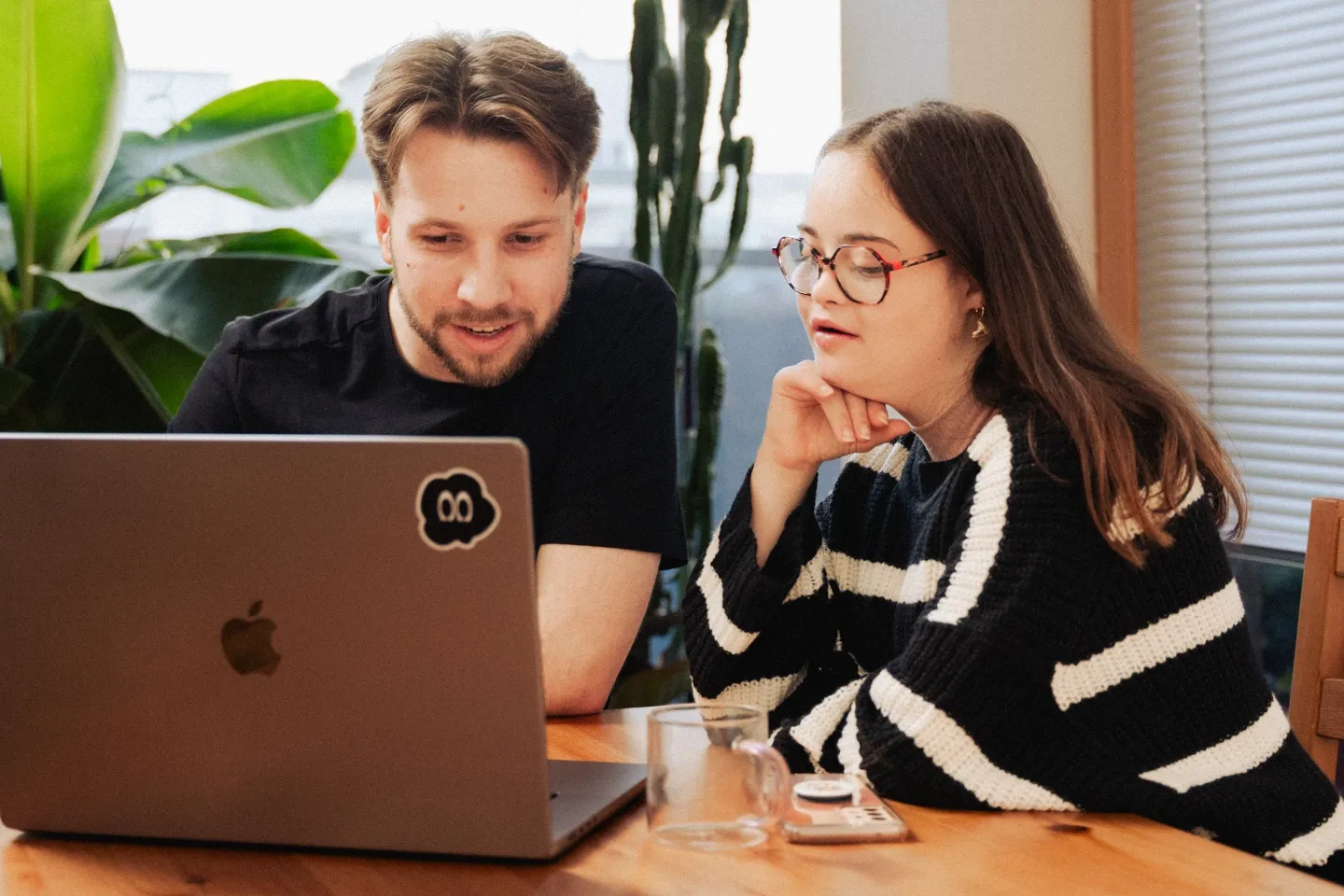Das Bild zeigt zwei Personen - eine mit und eine ohne Behinderung - die gemeinsam vor einem Laptop sitzen und arbeiten